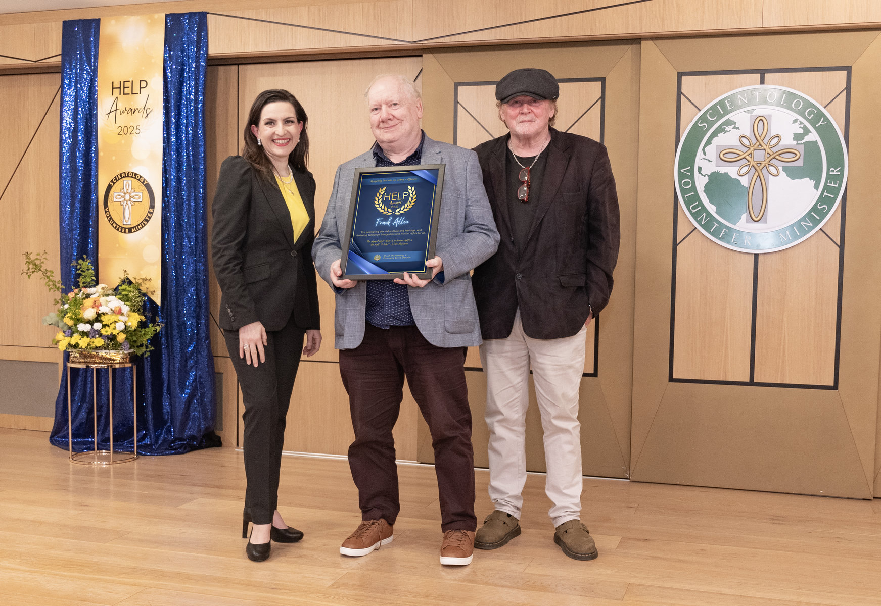 Hudebník Frank Allen přebírá cenu HELP, kterou mu na slavnostním ceremoniálu Scientologické církve a komunitního centra v Dublinu v roce 2025 předaly Diana Stahl a Francie Conway.