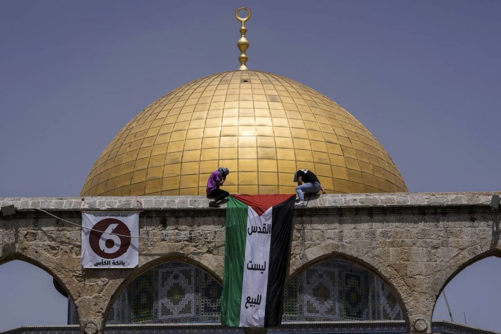 Maskovaní Palestinci vyvěšují státní vlajku během ramadánu v dubnu před svatyní Dome of the Rock v areálu mešity Al Aksá v jeruzalémském Starém městě.