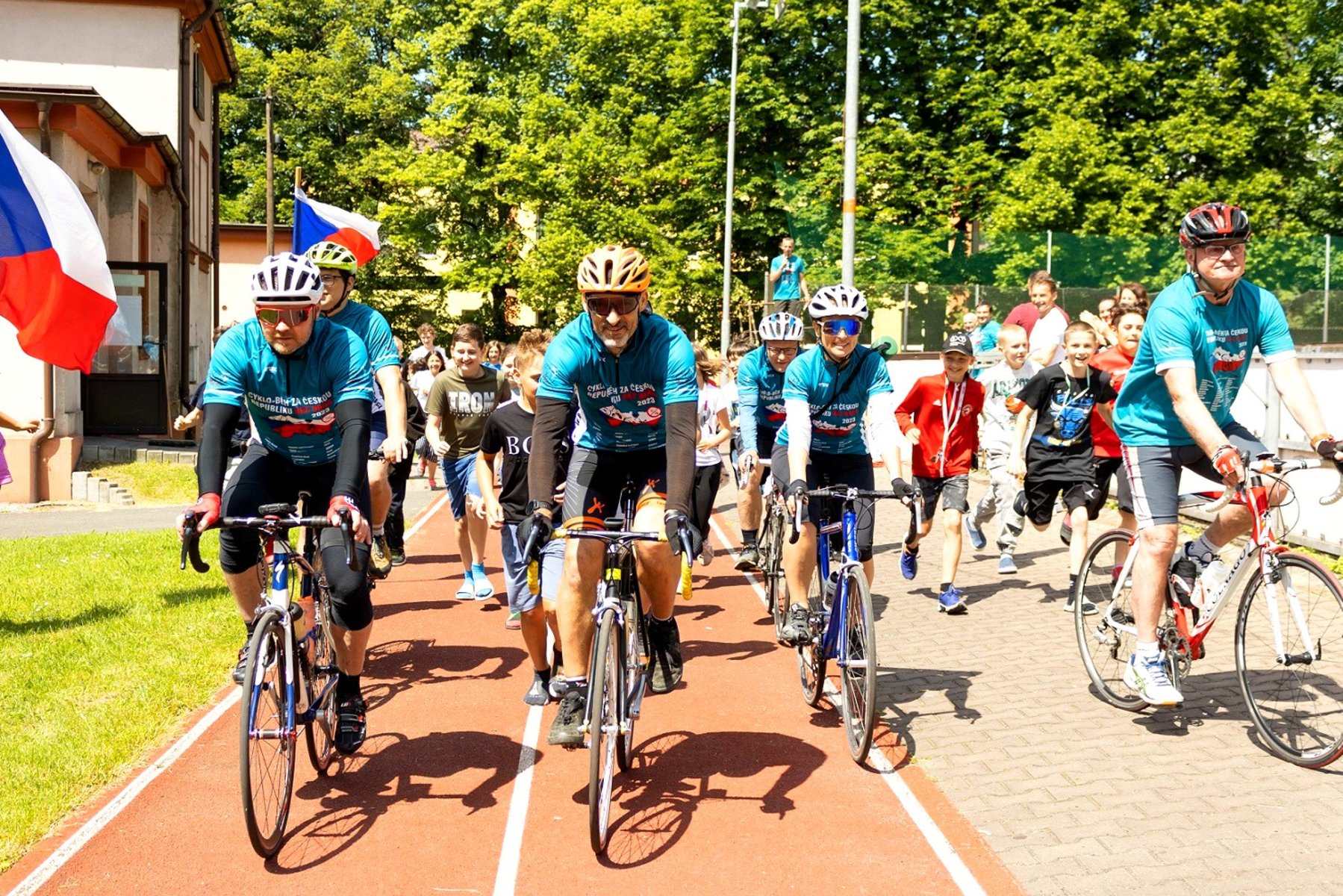 Tým Cyklo-běhu míří do dalšího města na jejich dvoutýdenním turné po celé České republice, v pozadí jsou děti.